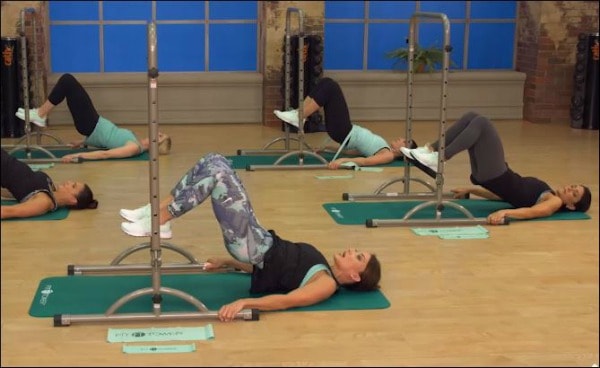 Cathe does glute squeezes using the Fit Tower bar
